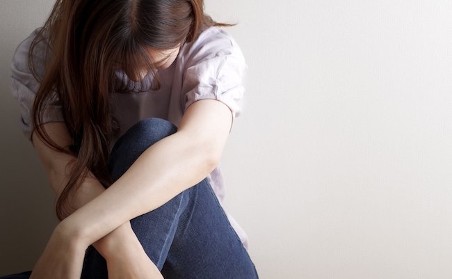 A young Japanese woman leaning against the wall and nod painfully