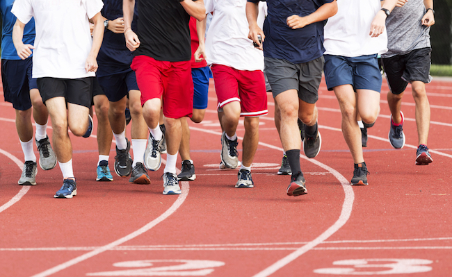 High school boys running in a large group on a red track during cross country practice.
