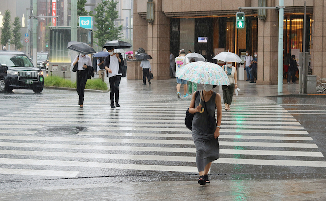 TOKYO, JAPAN - September 2, 2020: Photo taken in heavy rain focus on foreground of people using a crosswalk in Ginza during a heavy downpour. Mitsukoshi Department Store is in the background.