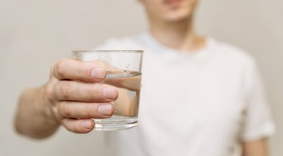 a young man in a white T-shirt holds a clear glass of clean drinking water