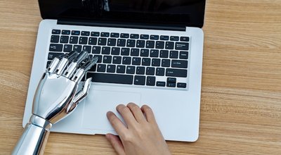 Robot hand and human hand using laptop.