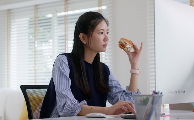 Asia people young woman MBA student gen Z girl work online on desk at home office multi tasking workforce hurry eat junk meal break time bite vegan meat burger diet. Stress relief by take out food.