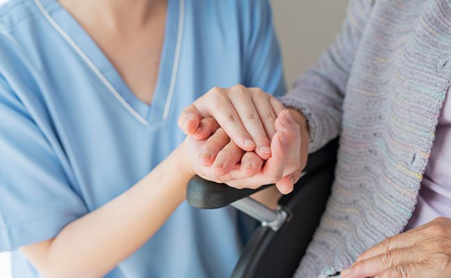 Senior woman in wheelchair indoors with Female Healthcare Professional Hand