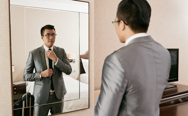 Young Asian businessman getting ready in front of big mirror