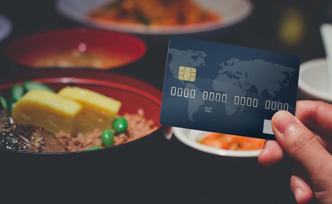 Hand holding Credit card on Japanese food in restaurant. Use credit card to pay for food. Shopping concept.