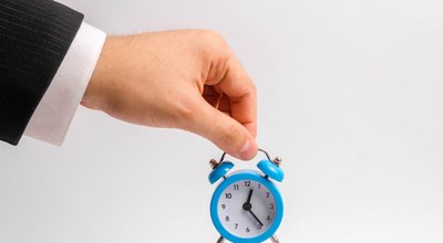 A businessman's hand holds a blue alarm clock on a white background. The concept of the flow of time, time to action. Hourly pay for work. Late for work and stay for part-time work. Time is money.