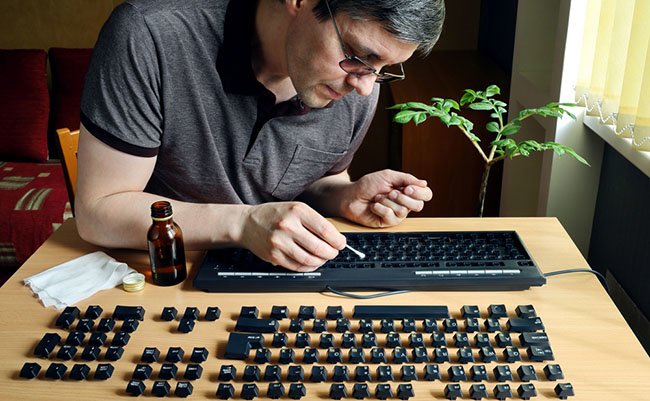 During isolation, a person is busy cleaning the dirty surface of a computer keyboard. He disassembled it to thoroughly clean the inaccessible parts