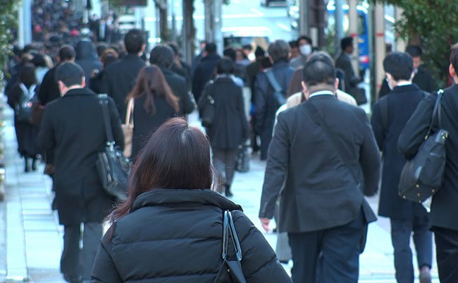 TOKYO, JAPAN - MAR 2020 : Back shot of unidentified crowd of people walking down the street in busy rush hour. Many commuters going to work. Japanese business man and woman, job and lifestyle concept.