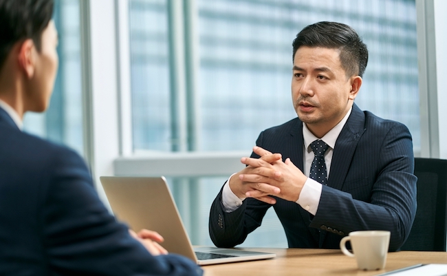 two asian business men sitting at desk face to face in modern office having a discussion