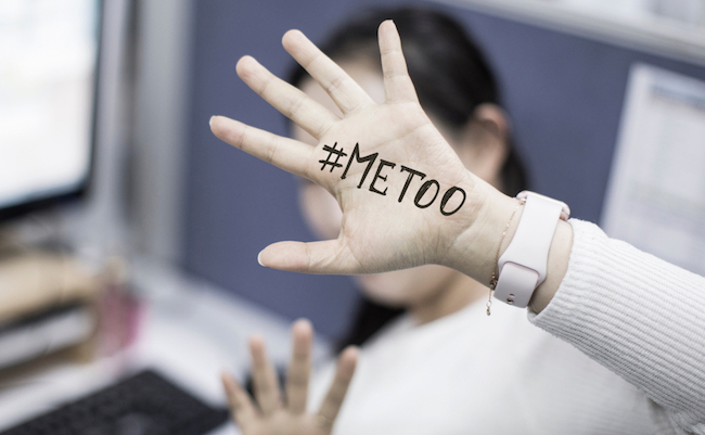 Close up portrait of unknown young woman covering her face w/ #Metoo hashtag word on palm of hand, taken in the office. Me too movement. Anti sexism protest against inappropriate behavior towards wome
