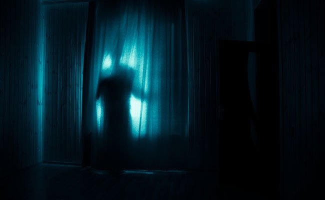 Horror silhouette in window with curtain inside bedroom at night. Horror scene. Halloween concept. Blurred silhouette of ghost