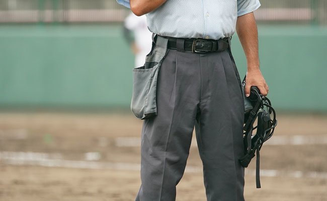 A ball umpire waits for the pitcher to practice pitching during a baseball game.