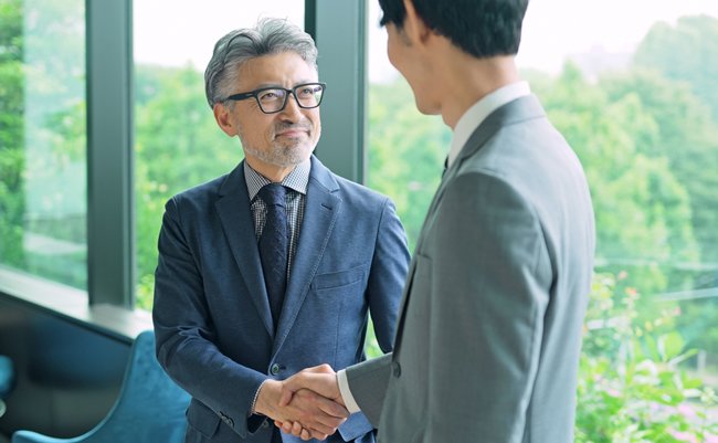 Middle aged executive man and young businessperson shaking hands in the office.