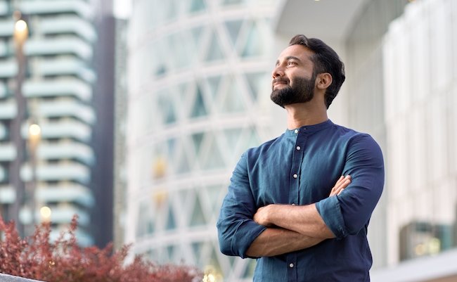Confident rich eastern indian business man executive standing in modern big city looking and dreaming of future business success, thinking of new goals, business vision and leadership concept.