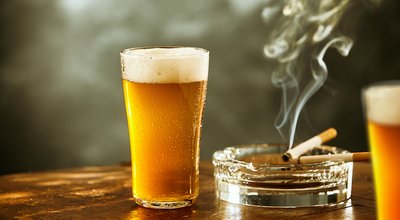 Ice cold lager or beer with a burning cigarette resting on a glass ashtray on a rustic wooden counter in a tavern, nightclub or pub, low angle close up