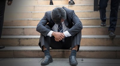 Depressed businessman bending down the head sitting on the stairs. Unemployed Middle edge man feel frustrated after business failure.