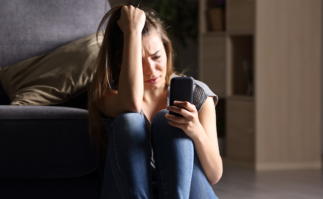 Front,View,Of,A,Sad,Teen,Checking,Phone,Sitting,On
