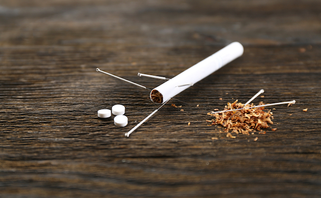 Acupuncture needles with cigarette on wooden background