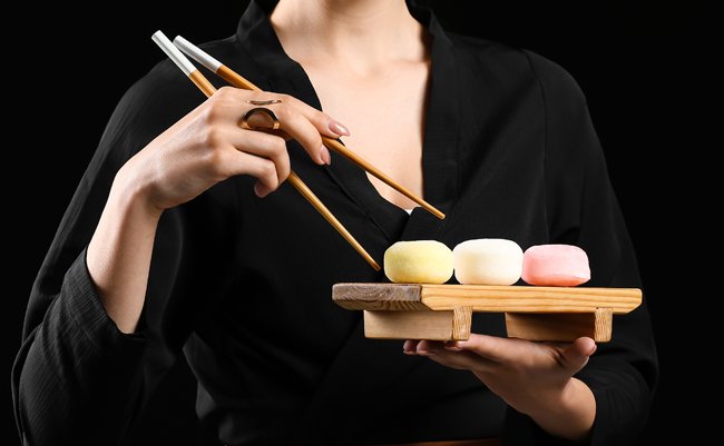 Beautiful young woman eating tasty Japanese mochi on black background with space for text