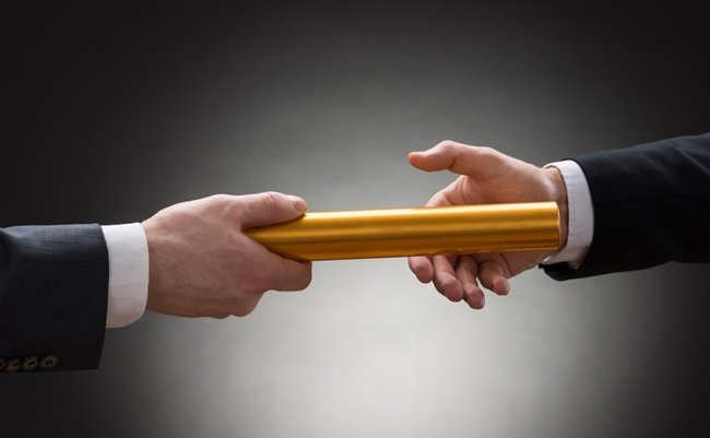 Close-up,Of,Two,Businessman's,Hand,Passing,A,Golden,Relay,Baton