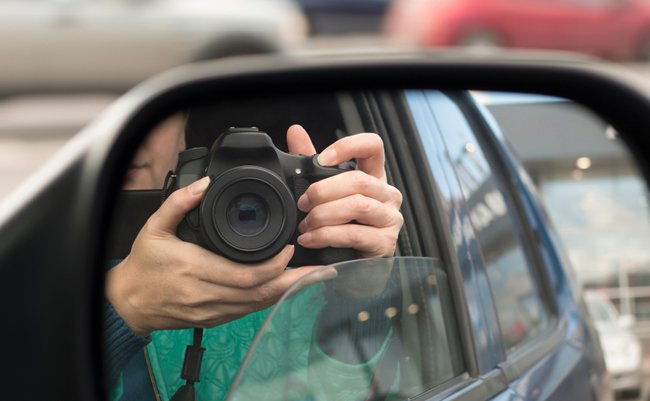 Hidden photographing. Reflection in car mirror of woman with camera. Paparazzi concept