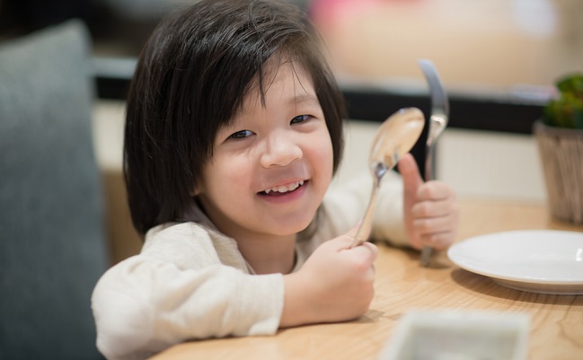 Cute,Asian,Child,Holding,A,Spoon,And,Fork,With,Empty