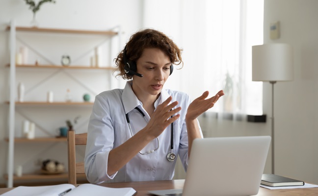 Female,General,Practitioner,Wears,White,Coat,And,Headset,Speaking,Videoconferencing
