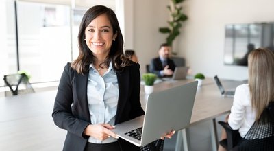 Portrait,Of,Smiling,Female,Entrepreneur,Holding,A,Laptop,With,Team