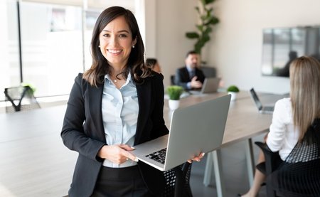 Portrait,Of,Smiling,Female,Entrepreneur,Holding,A,Laptop,With,Team