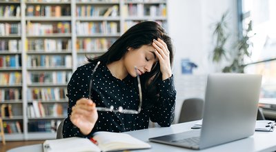 Headache while working. Stress. Young caucasian woman, manager or student, upset and tired from work sits at the desk, holding her head