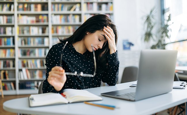 Headache while working. Stress. Young caucasian woman, manager or student, upset and tired from work sits at the desk, holding her head
