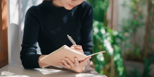 Asian,Working,Woman,Wearing,Black,Shirt,And,Writing,Journal,On