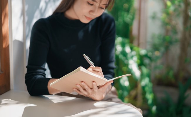 Asian,Working,Woman,Wearing,Black,Shirt,And,Writing,Journal,On