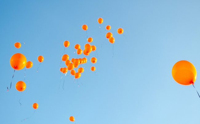 Orange,Balloons,Rising,To,The,Sky,,Balloons,Released,Against,Blue