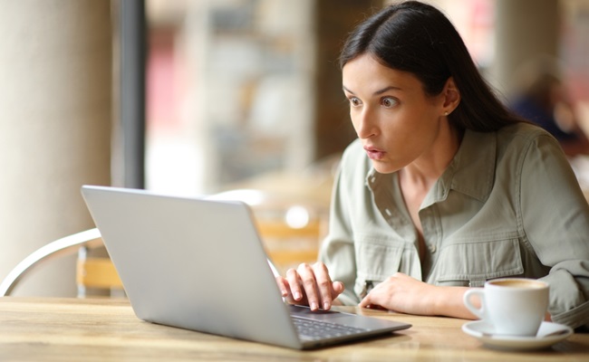 Amazed,Woman,Watching,Surprising,Content,On,Laptop,In,A,Restaurant