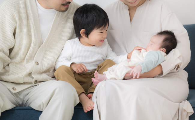 A,Japanese,Couple,Holds,Their,Small,Children,By,The,Window