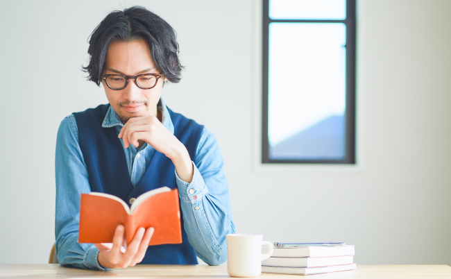 Young,Man,Reading,A,Book,In,His,Study,At,Home