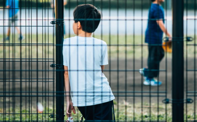 A,Japanese,Boy,Leans,Against,A,Steel,Net,Fence,At