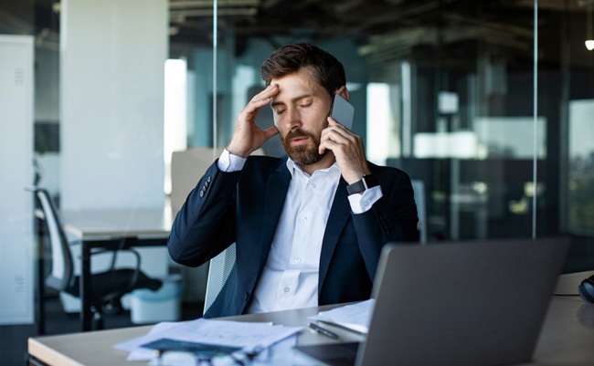 Concerned,Male,Entrepreneur,Talking,On,Cellphone,And,Touching,Head,In