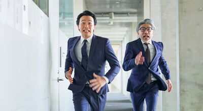 Two,Business,People,Running,Through,The,Corridor,Of,A,Building