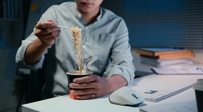 Young,Businessman,Eating,Instant,Noodles,While,Working,Late,At,The