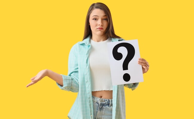 Wondering,Young,Woman,With,Paper,Question,Mark,On,Yellow,Background