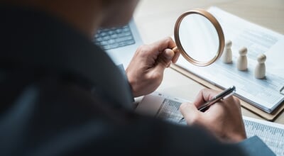Businessman,Using,Magnifying,Glass,To,Review,Financial,Documents,On,Desk.