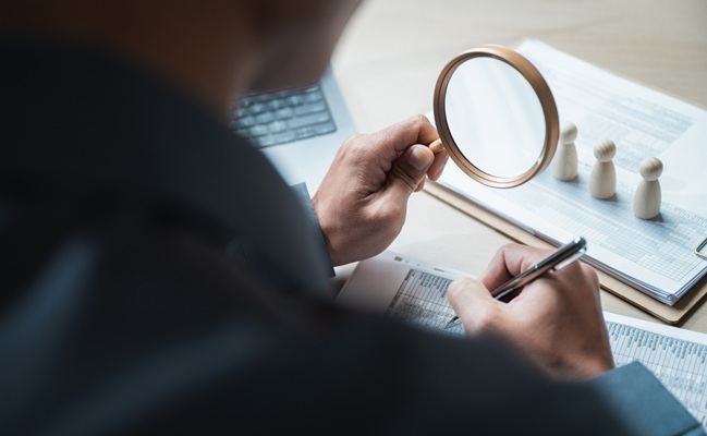 Businessman,Using,Magnifying,Glass,To,Review,Financial,Documents,On,Desk.