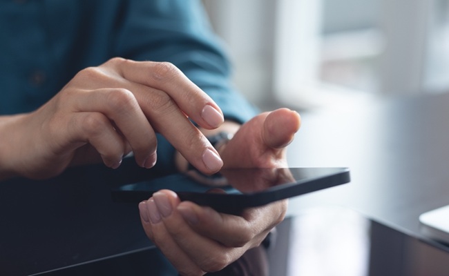 Woman,Using,Mobile,Phone,With,Laptop,Computer,On,Office,Table.
