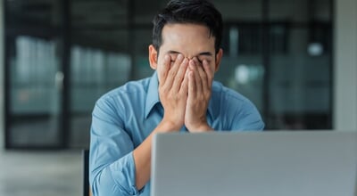 Asian,Businessman,Covering,Face,With,Hands,At,Office,Desk,,Feeling