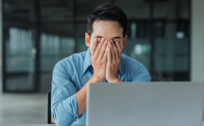 Asian,Businessman,Covering,Face,With,Hands,At,Office,Desk,,Feeling