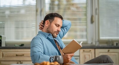 Man,Reading,A,Book,At,A,Kitchen,Table,,Enjoying,Coffee