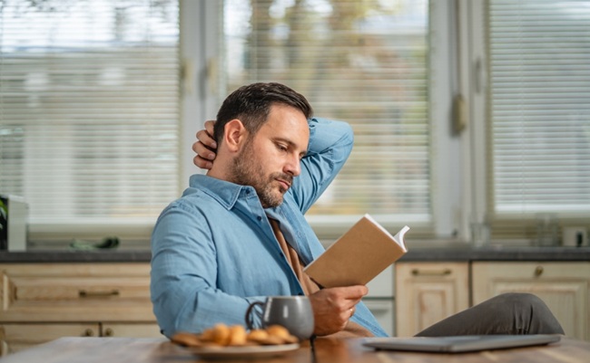 Man,Reading,A,Book,At,A,Kitchen,Table,,Enjoying,Coffee
