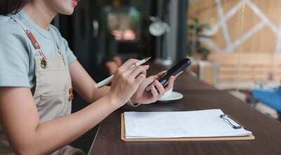 Asian,Barista,Taking,Orders,And,Managing,Inventory,Using,A,Smartphone